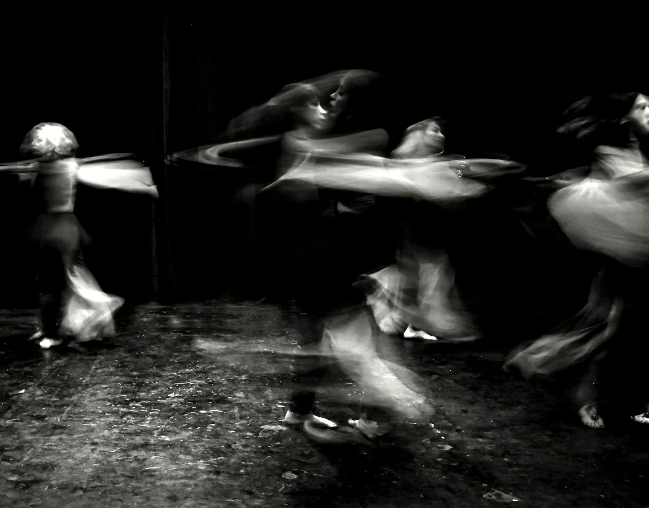 Black and white image capturing dancers in motion on stage, creating an abstract blur effect.