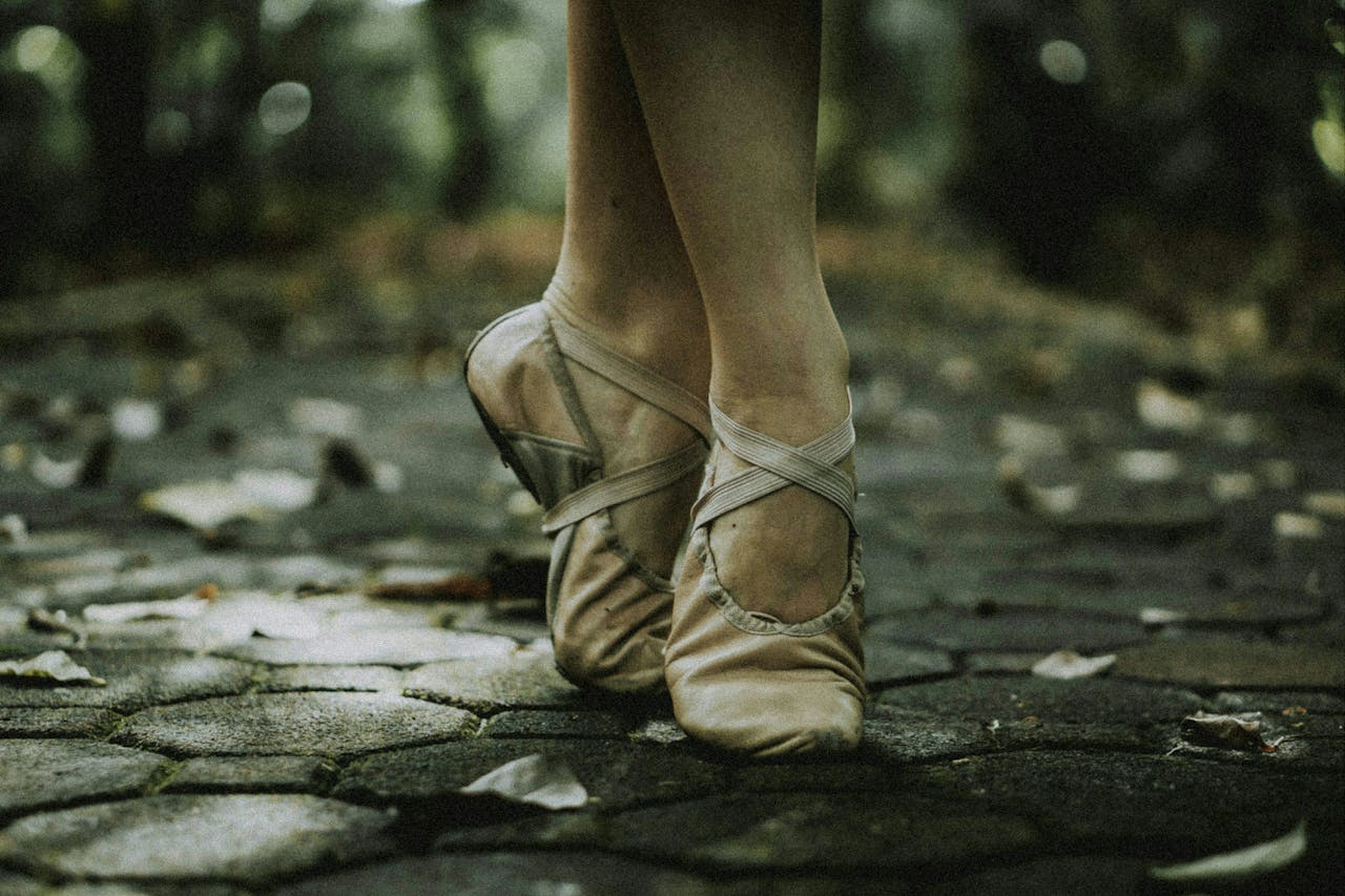 Elegant ballerina in pointe shoes performing on an outdoor stone pathway, captured in a low angle shot.