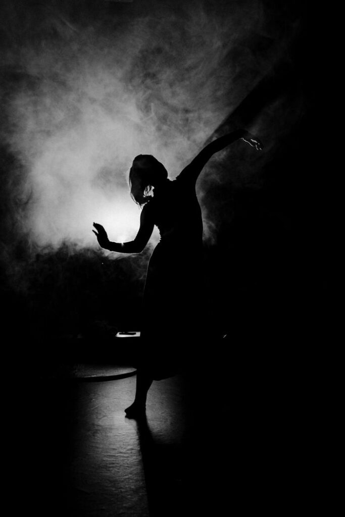pexels photo 5135102 Black and white silhouette of a woman dancer performing on a smoky stage.