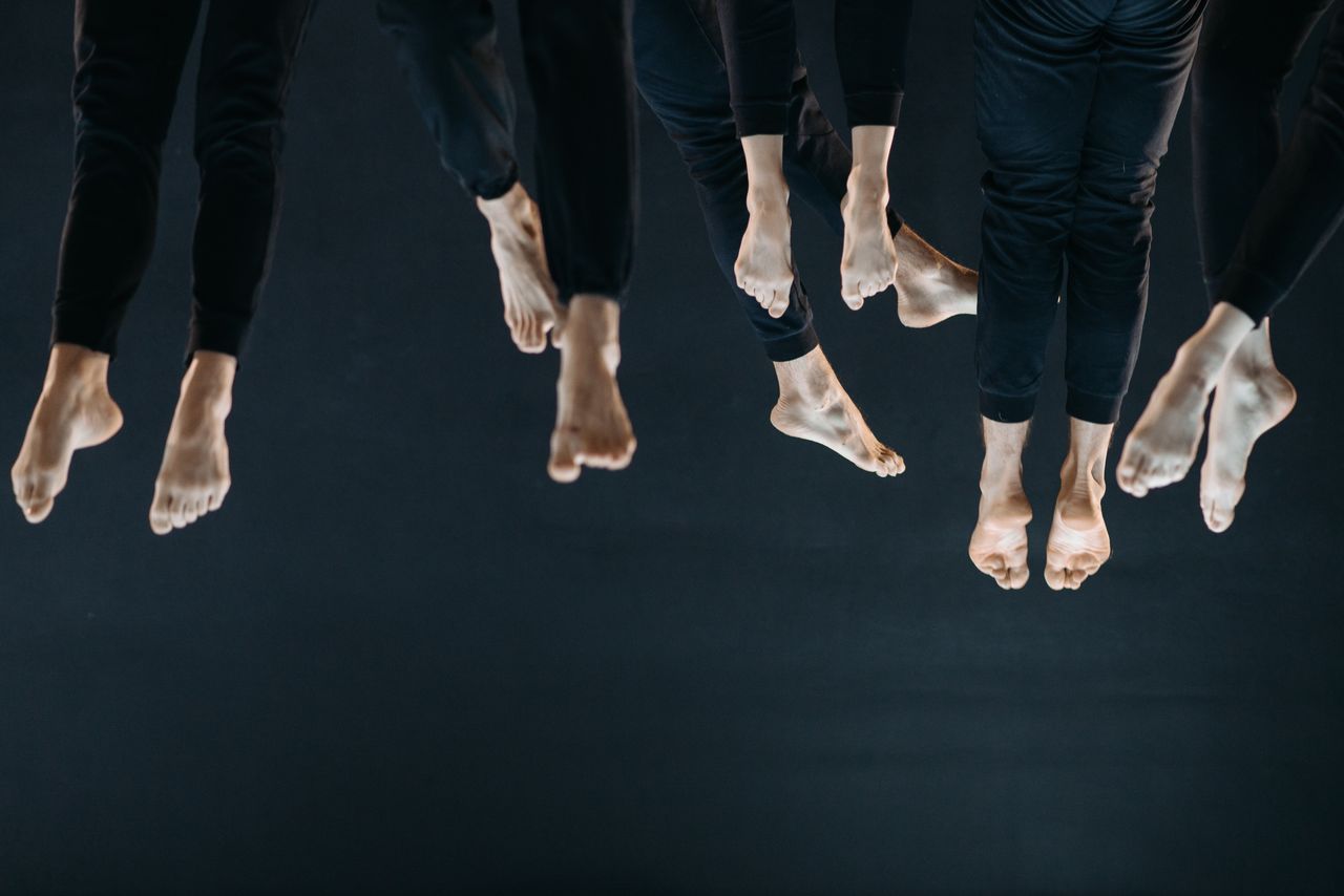 Elegant dancers in black leggings showing graceful, barefoot choreography on black background.